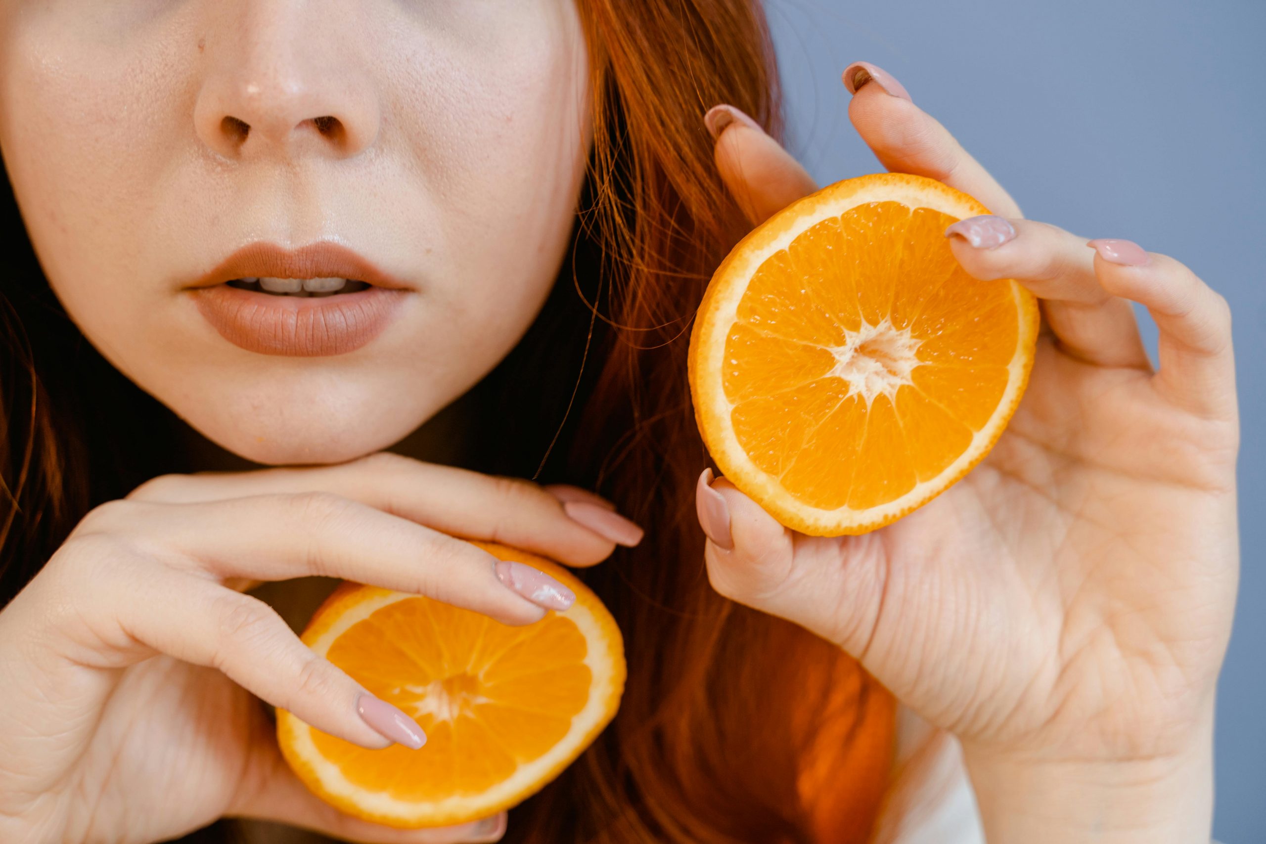 A close-up image of a woman holding juicy orange slices in her hands.